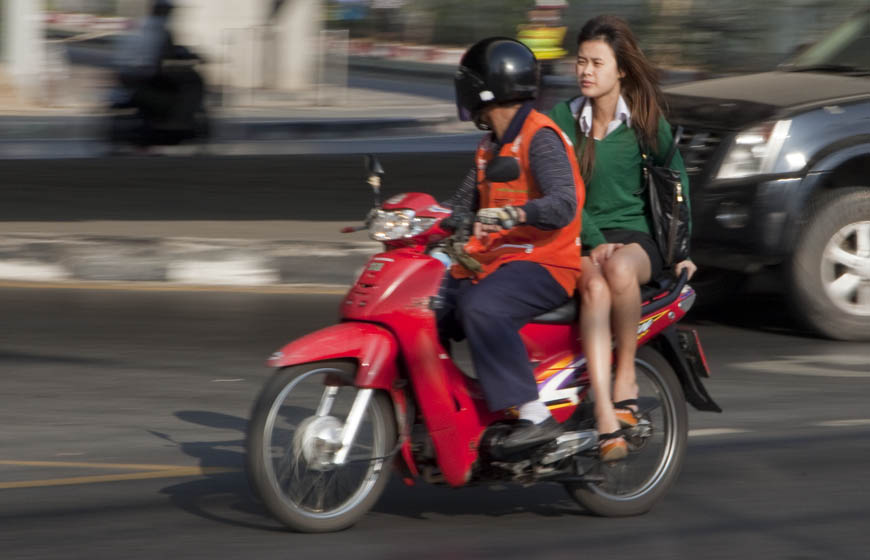 woman modestly rides a Bangkok motorcycle tax.
