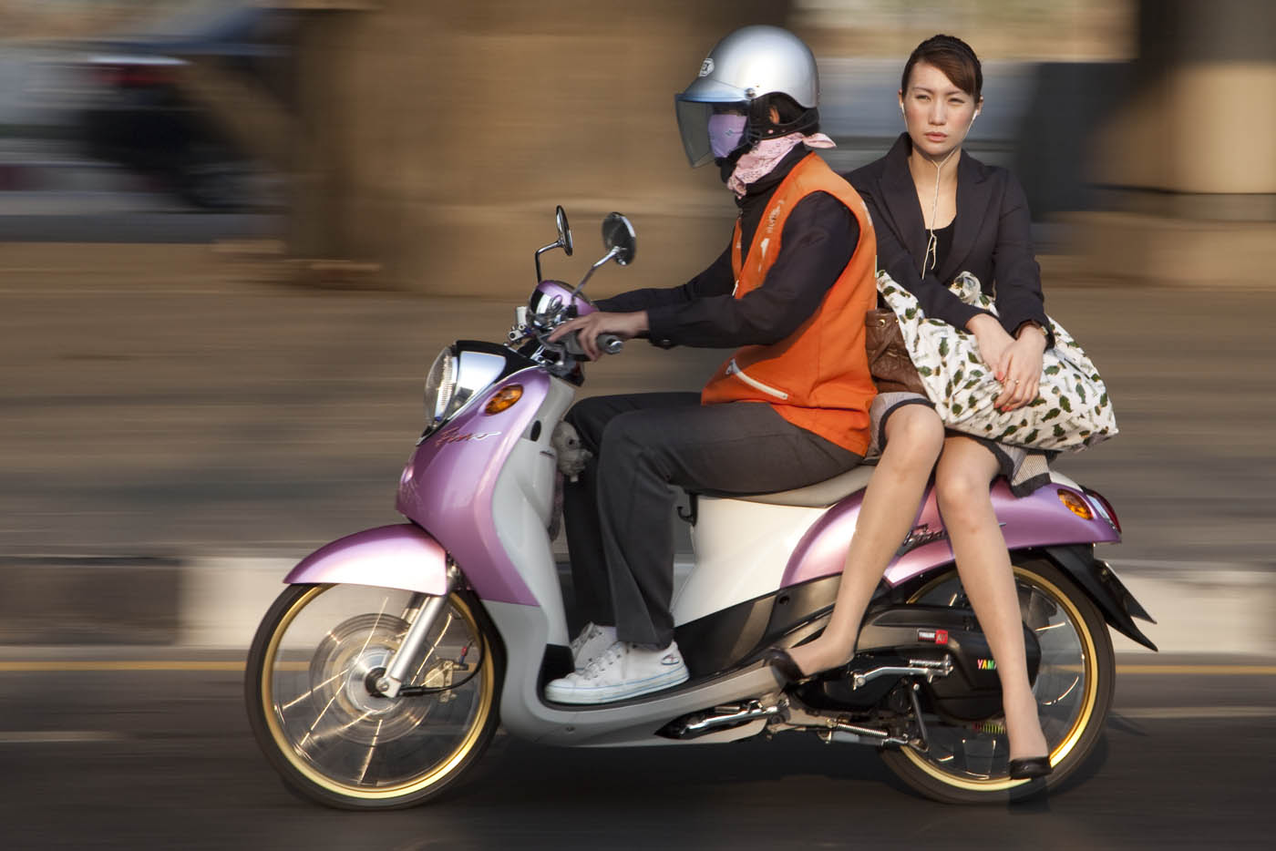 A woman listens to her I-pod while riding on a Bangkok motorcycle taxi.